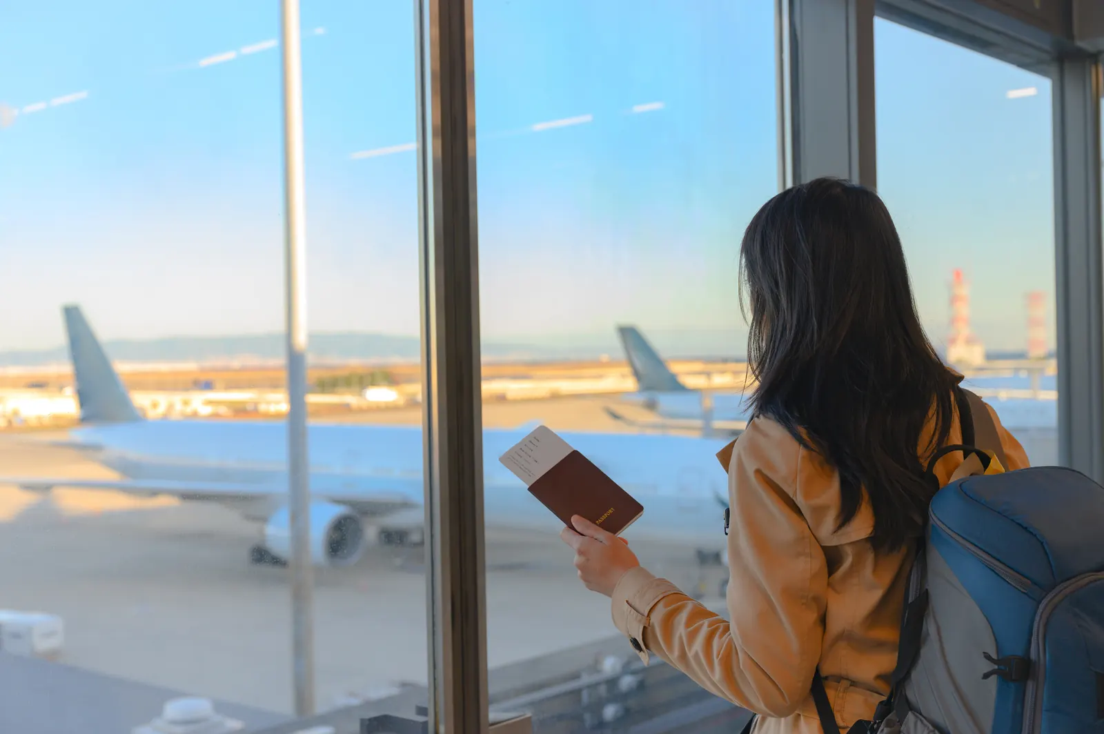 Estudiante con el pasaporte en la mano frente al ventanal de un aeropuerto
